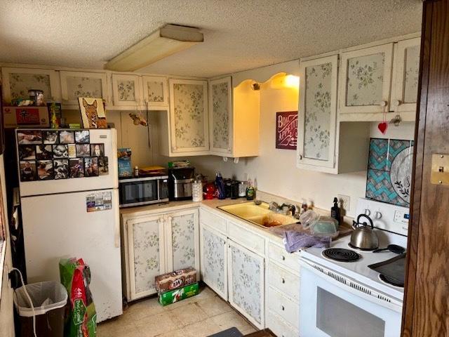 kitchen featuring a textured ceiling, white appliances, light countertops, and a sink