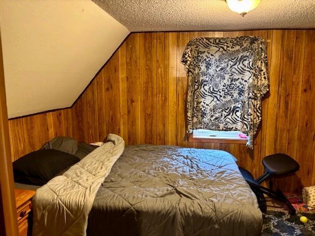 bedroom featuring wood walls, a textured ceiling, and vaulted ceiling