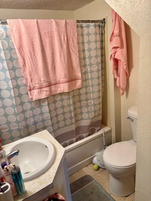 bathroom featuring shower / bathtub combination with curtain, a textured ceiling, vanity, and toilet
