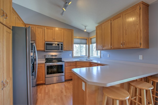 kitchen with a peninsula, light countertops, a sink, vaulted ceiling, and stainless steel appliances