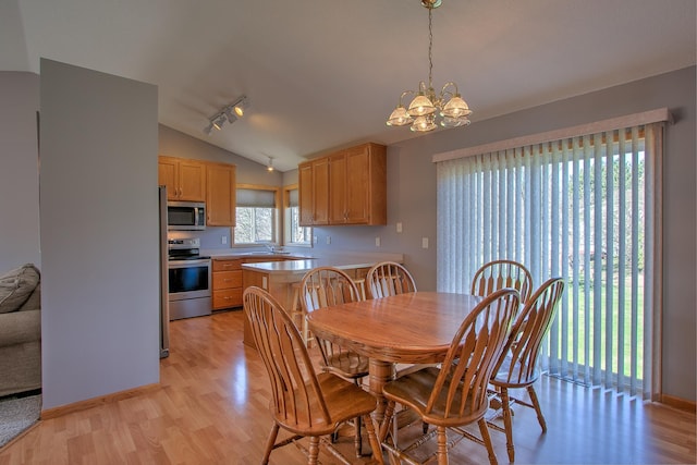 dining room featuring an inviting chandelier, track lighting, light wood-style flooring, and lofted ceiling
