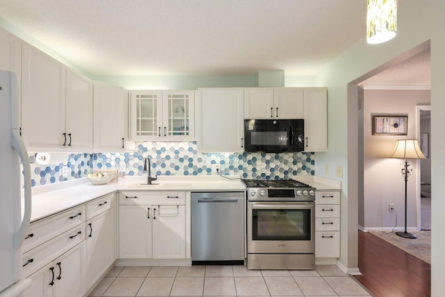 kitchen featuring appliances with stainless steel finishes, light countertops, decorative backsplash, glass insert cabinets, and white cabinetry
