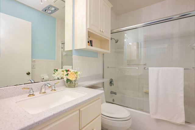 full bath featuring toilet, bath / shower combo with glass door, vanity, and tile walls