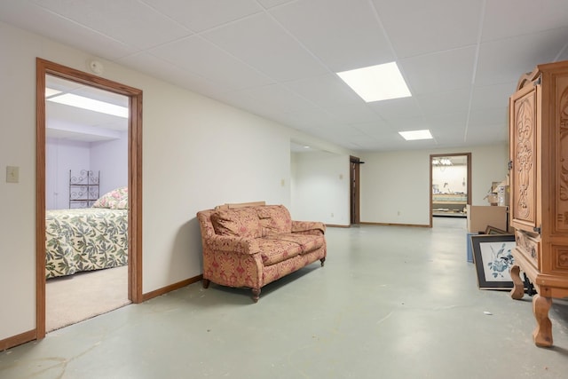 living area featuring a drop ceiling, baseboards, and finished concrete floors