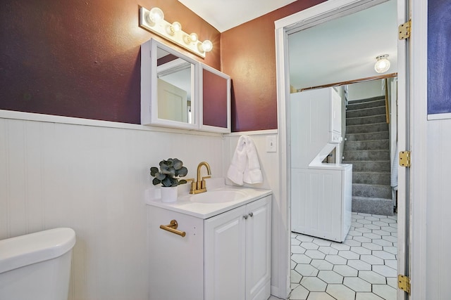 bathroom with toilet, vanity, a wainscoted wall, and tile patterned floors