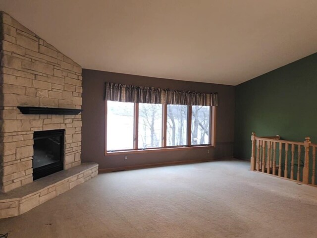 unfurnished living room featuring carpet floors, vaulted ceiling, and a stone fireplace