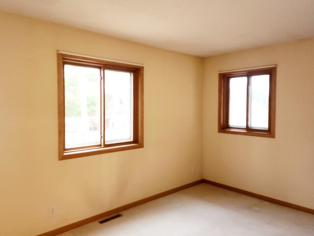 spare room with a healthy amount of sunlight, baseboards, visible vents, and light colored carpet