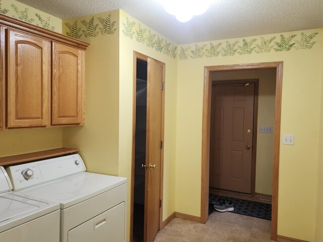 clothes washing area with cabinet space, a textured ceiling, baseboards, and washing machine and clothes dryer