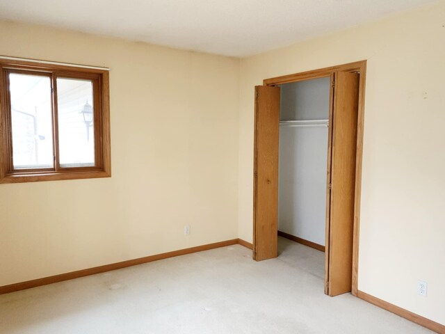 unfurnished bedroom featuring light colored carpet, baseboards, and a closet