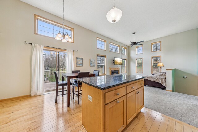 kitchen with a lit fireplace, a healthy amount of sunlight, light wood finished floors, and ceiling fan with notable chandelier