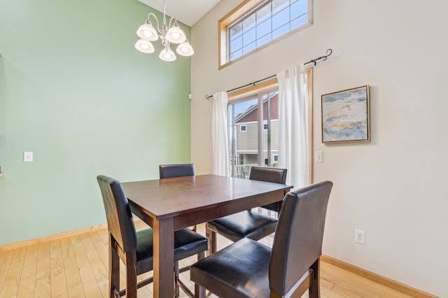 dining area with light wood-style floors, baseboards, a high ceiling, and a chandelier