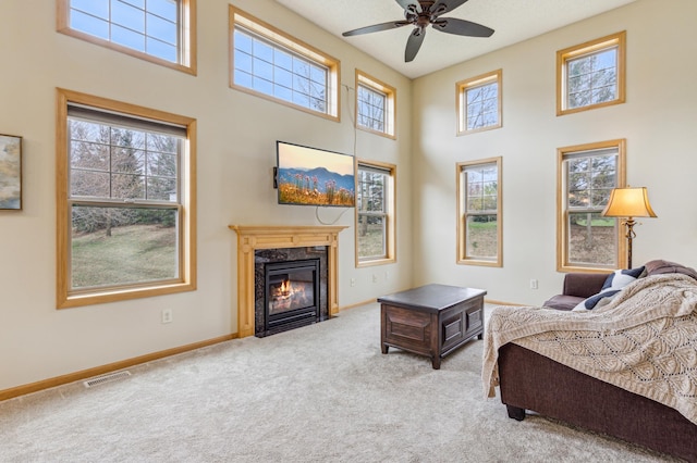 carpeted living room with a wealth of natural light, a premium fireplace, ceiling fan, and a towering ceiling