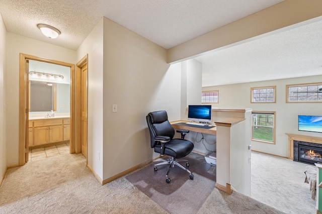 office space featuring a fireplace, baseboards, light carpet, and a textured ceiling