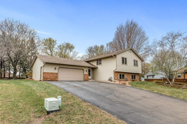 split level home featuring a garage, driveway, a front lawn, and brick siding