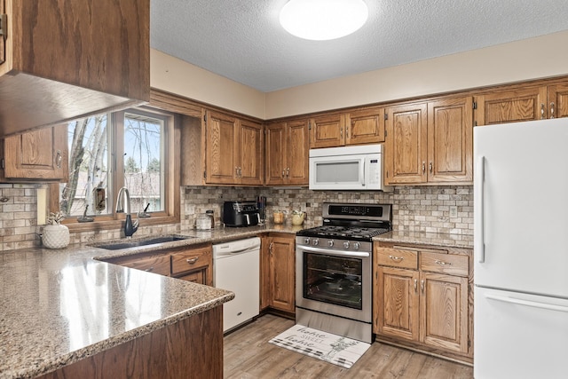 kitchen with white appliances, a textured ceiling, brown cabinets, a sink, and backsplash
