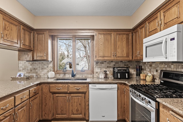 kitchen with white appliances, brown cabinetry, and a sink