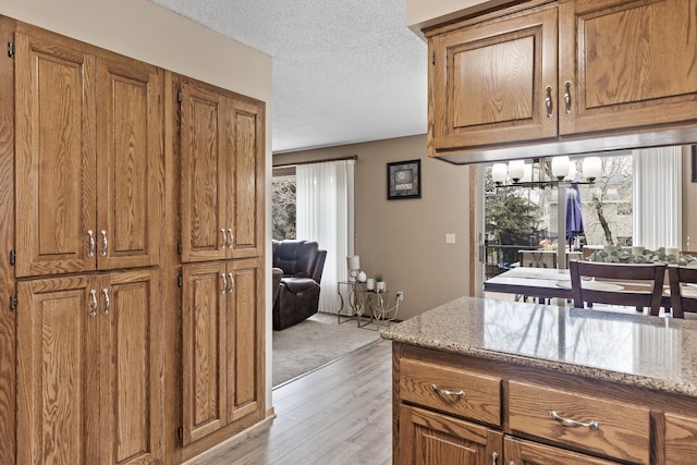 kitchen featuring brown cabinetry, light stone countertops, light wood-style floors, a textured ceiling, and a chandelier