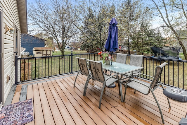 wooden terrace featuring an outdoor structure, a trampoline, a yard, and outdoor dining space