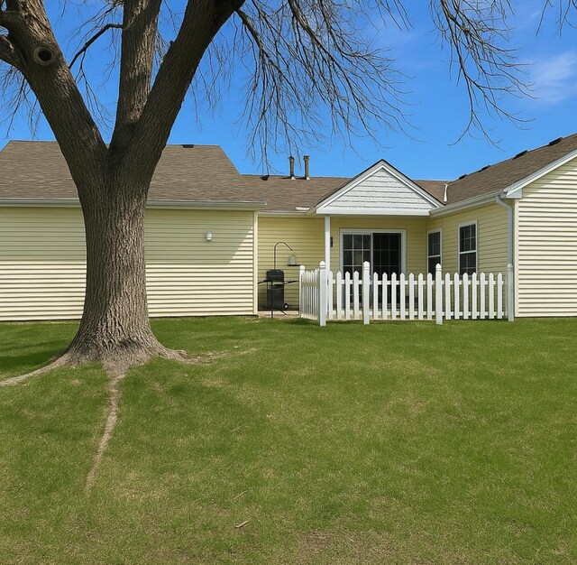 rear view of house featuring a lawn and fence