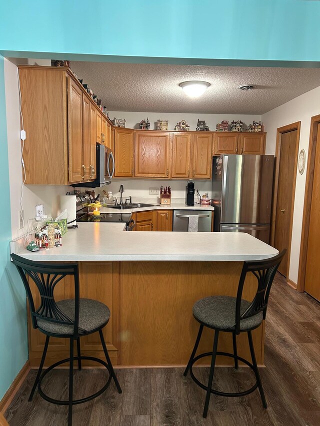 kitchen with brown cabinets, a sink, stainless steel appliances, a peninsula, and dark wood-style floors