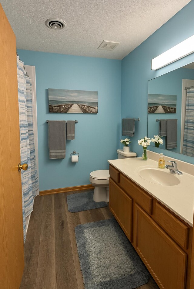 bathroom with a textured ceiling, visible vents, wood finished floors, vanity, and toilet