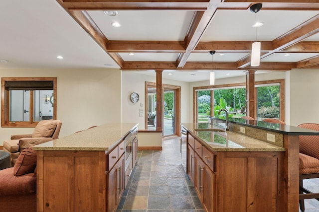 7250 Jubert Ln, Corcoran, MN 55340 - kitchen featuring an island with sink, brown cabinets, a sink, stone tile flooring, and open floor plan