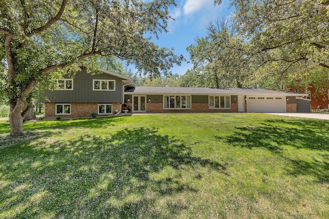 split level home with french doors, brick siding, an attached garage, and a front lawn
