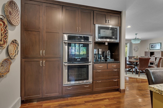 kitchen featuring appliances with stainless steel finishes, light wood finished floors, stone counters, recessed lighting, and dark brown cabinets