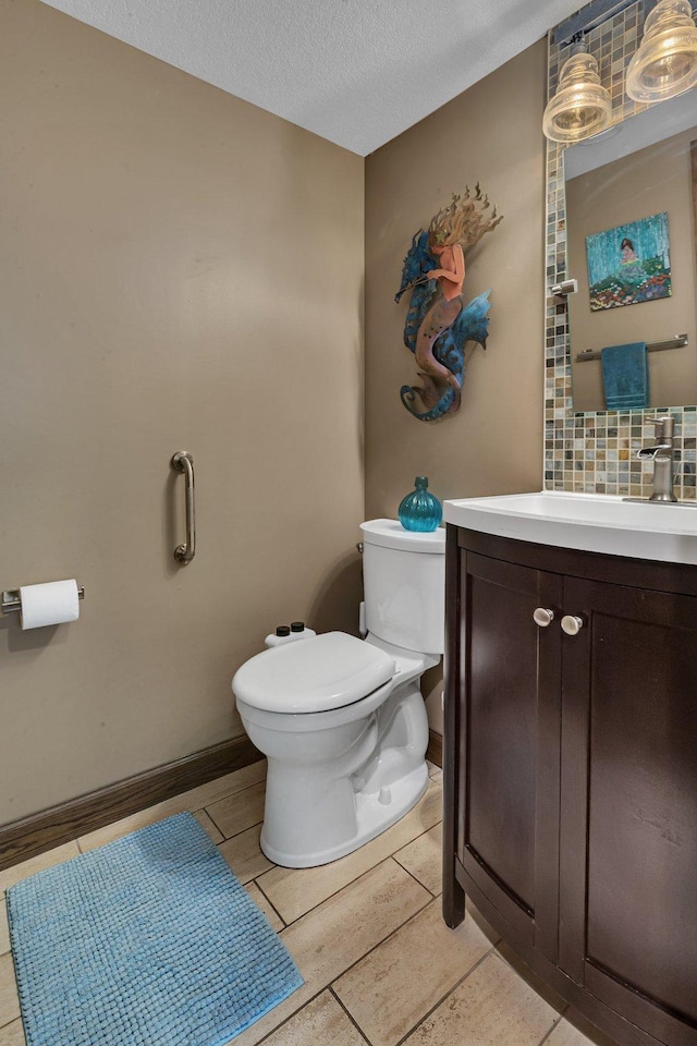 bathroom featuring toilet, vanity, a textured ceiling, tasteful backsplash, and baseboards
