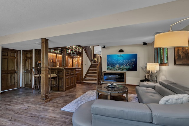 living room with dark wood-type flooring, decorative columns, bar, and stairs