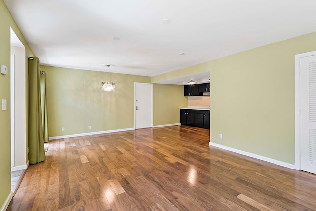 unfurnished living room with wood finished floors, a chandelier, and baseboards