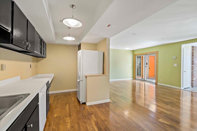 kitchen featuring dark cabinets, freestanding refrigerator, light wood-type flooring, and baseboards