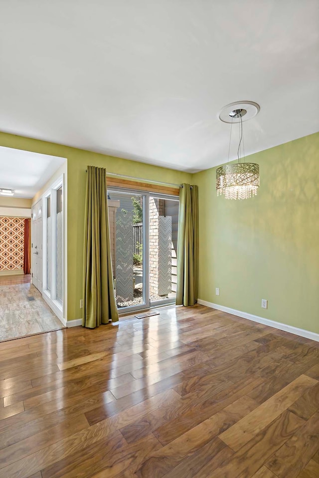 spare room featuring a chandelier, hardwood / wood-style floors, and baseboards