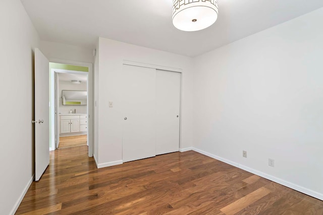 unfurnished bedroom featuring wood finished floors, a closet, baseboards, and a sink