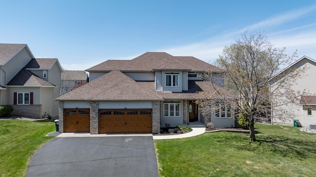 traditional-style house featuring a garage, aphalt driveway, a front yard, brick siding, and a shingled roof