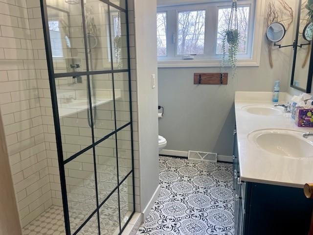full bathroom featuring a stall shower, baseboards, double vanity, and tile patterned flooring