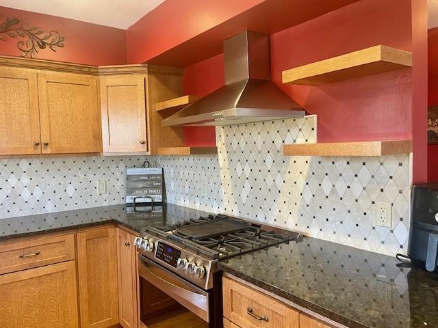 kitchen with stainless steel range with gas stovetop, wall chimney exhaust hood, open shelves, and decorative backsplash