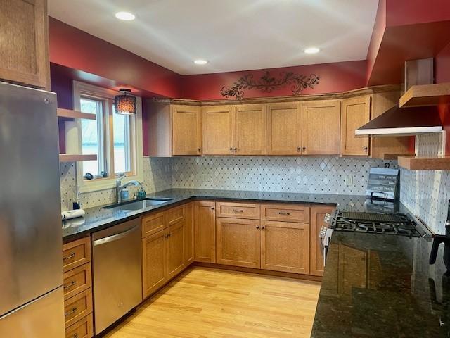 kitchen featuring appliances with stainless steel finishes, a sink, light wood-style flooring, dark stone countertops, and recessed lighting