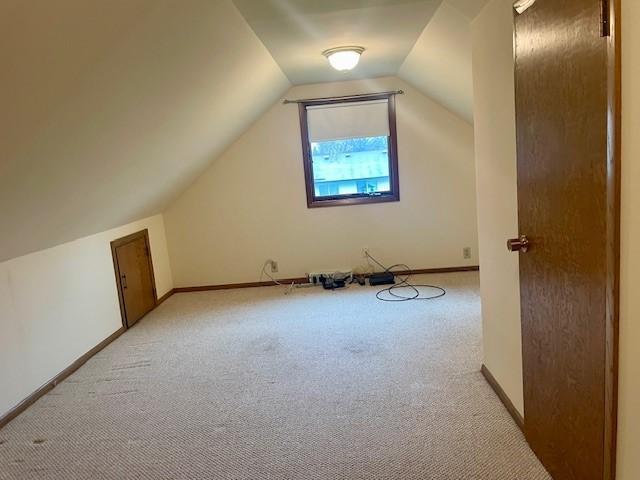 additional living space with light carpet, lofted ceiling, and baseboards
