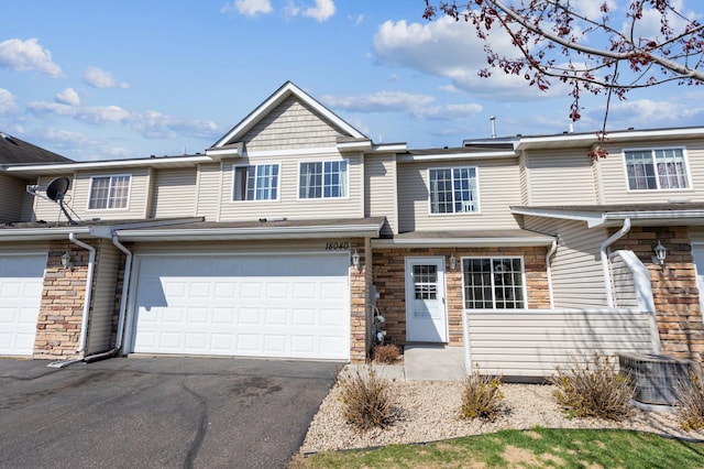 multi unit property featuring an attached garage, central AC unit, stone siding, and aphalt driveway
