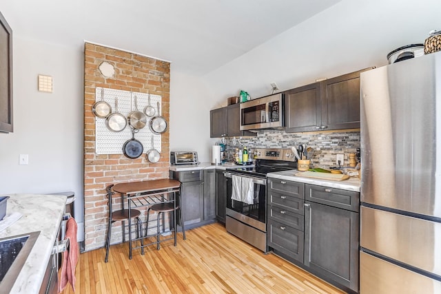 1976 Iglehart Ave, Saint Paul, MN 55104 - kitchen featuring appliances with stainless steel finishes, light countertops, lofted ceiling, light wood-style flooring, and backsplash
