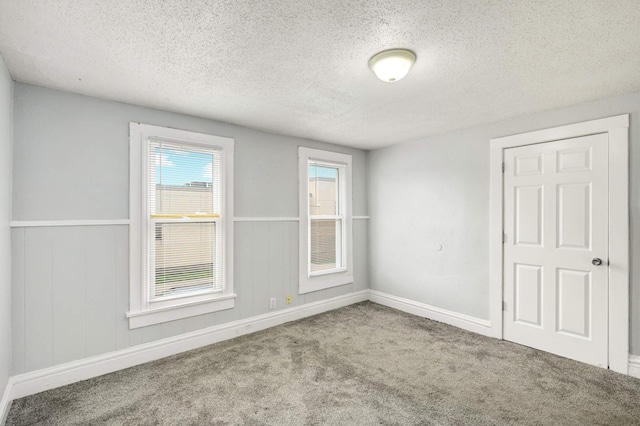 empty room featuring a textured ceiling, carpet flooring, wainscoting, and baseboards