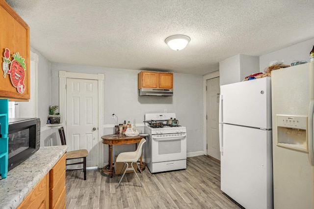 kitchen featuring light wood finished floors, a textured ceiling, under cabinet range hood, and white appliances