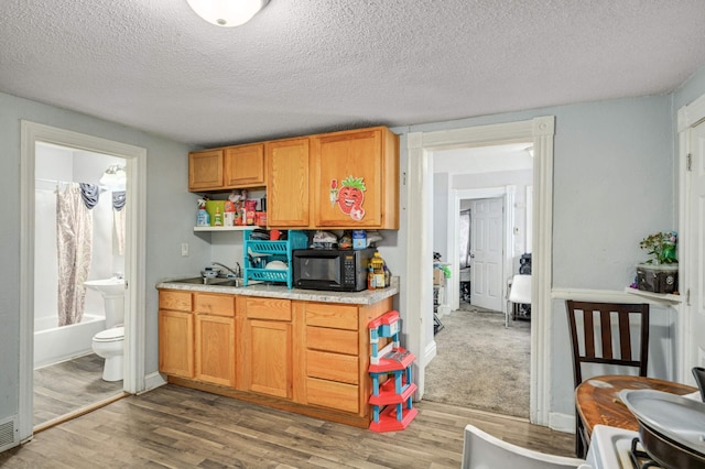 kitchen with open shelves, light wood-type flooring, black microwave, light countertops, and a textured ceiling
