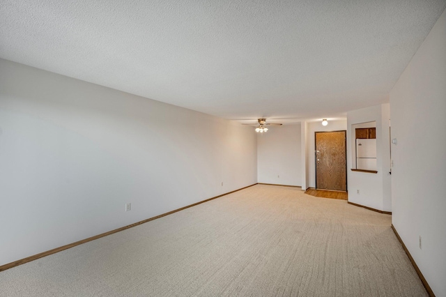 empty room with baseboards, ceiling fan, a textured ceiling, and light colored carpet