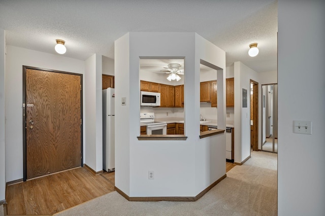 kitchen featuring ceiling fan, white appliances, brown cabinetry, a peninsula, and baseboards