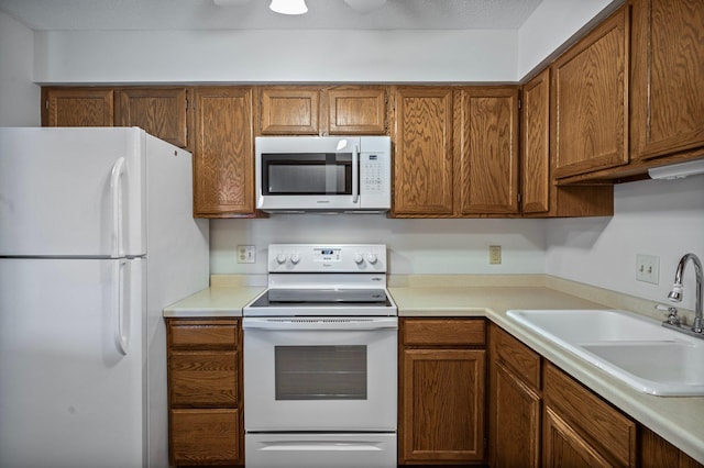 kitchen featuring brown cabinetry, white appliances, light countertops, and a sink