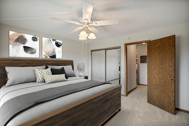 bedroom featuring a textured ceiling, light colored carpet, ceiling fan, baseboards, and a closet