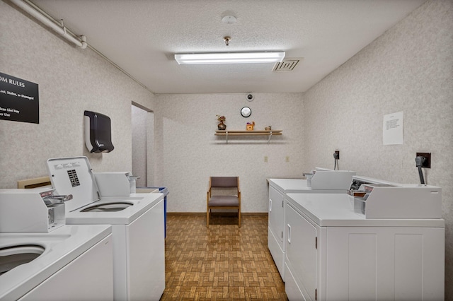 shared laundry area with a textured ceiling, visible vents, brick patterned floor, and washer and clothes dryer