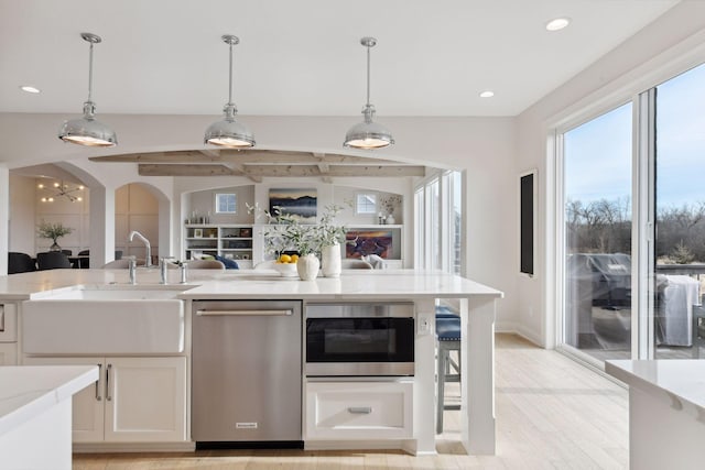 kitchen featuring a sink, built in microwave, open floor plan, dishwasher, and hanging light fixtures